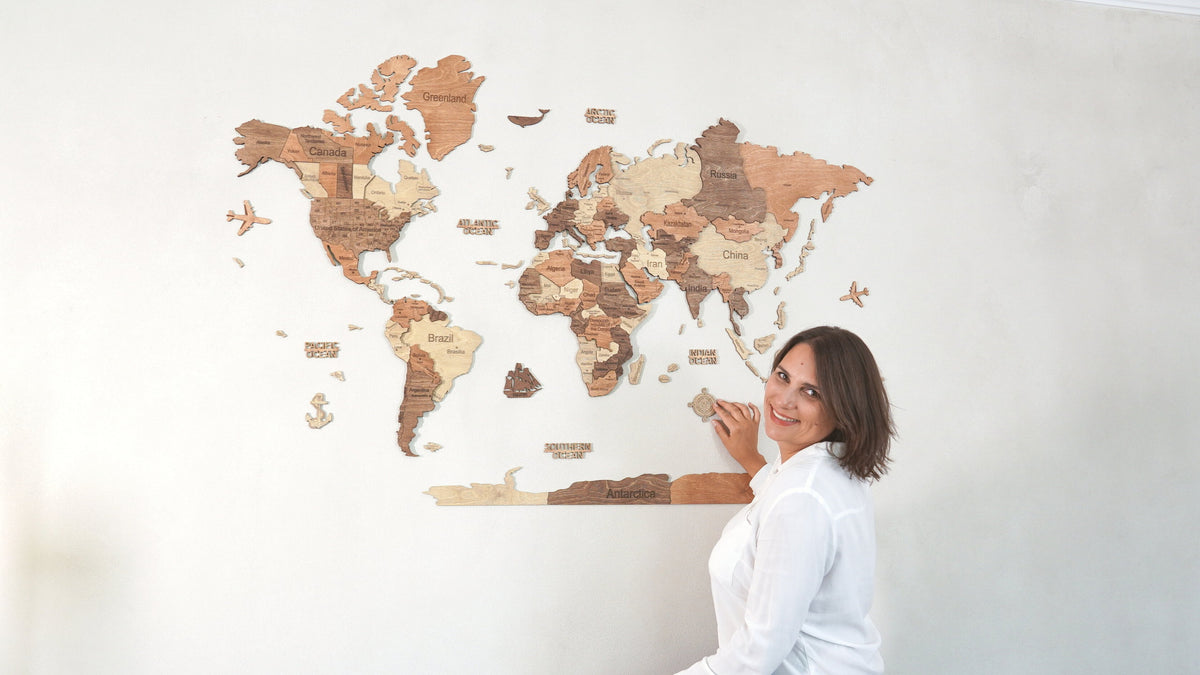 Une femme ajuste la rose des vents d'une carte du monde en bois 3D fixée au mur